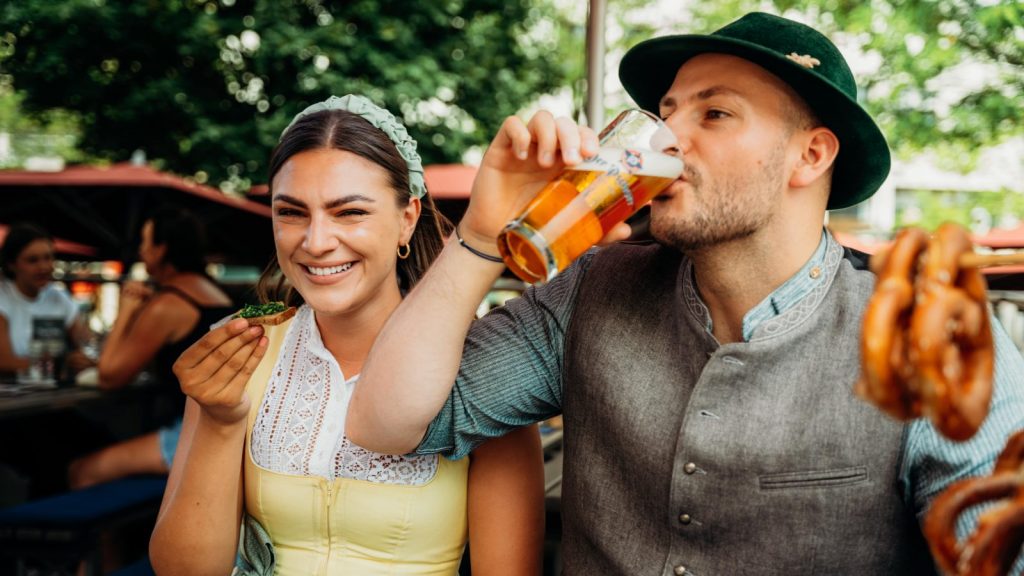 Paar im biergarten am marienplatz beim der pschorr münchen – mann trinkt pschorr bier, frau genießt brotzeit mit schnittlauchbrot.